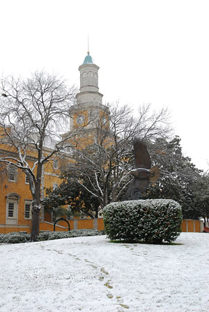 Administration building with eagle statue in foreground. Ground and bushes are lightly covered in snow.