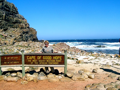 Mary Ellen Scribner at the Cape of Good Hope. Ocean in the background, rocky cliffs building on the left and rounded boulders the site of watermelons scatter around the beach