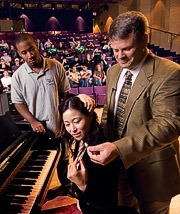 Kris Chesky hands and earplug to  a student, seated at a piano.