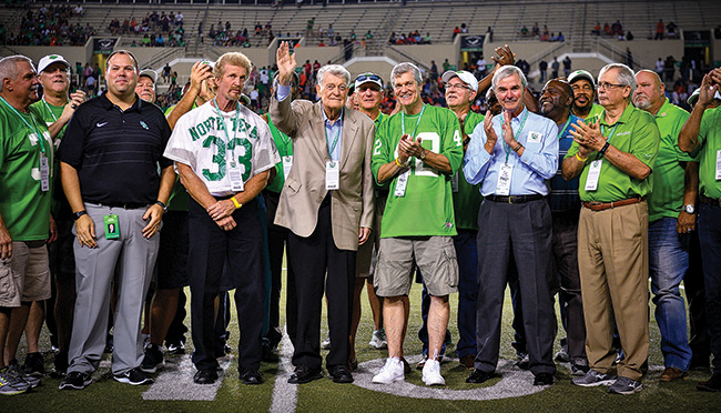 Legendary Mean Green head coach Hayden Fry (waving) and some of his former Mean Green players were honored at halftime of the UNT game against UTSA in October. Fry led the football team from 1973 to 1978, during which time the Mean Green had four straight winning seasons, including a 10-win season and a national ranking in 1977. (Photo by Michael Clements)