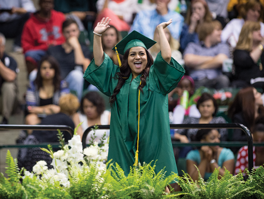 UNT student on stage at commencement wear cap and gown regalia