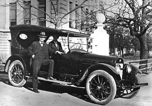 President Bruce standing beside a car with Mrs. Bruce sitting in the passenger seat.