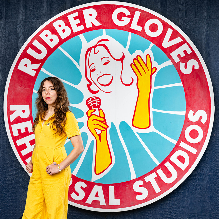 Claire Morales posing in front of the Rubber Gloves logo