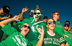 Students dressed in green cheering at a football game.