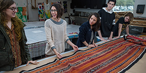 Lesli Robertson and her students discuss Bedouin weavings she brought back from Kuwait. (Photo by Ahna Hubnik)