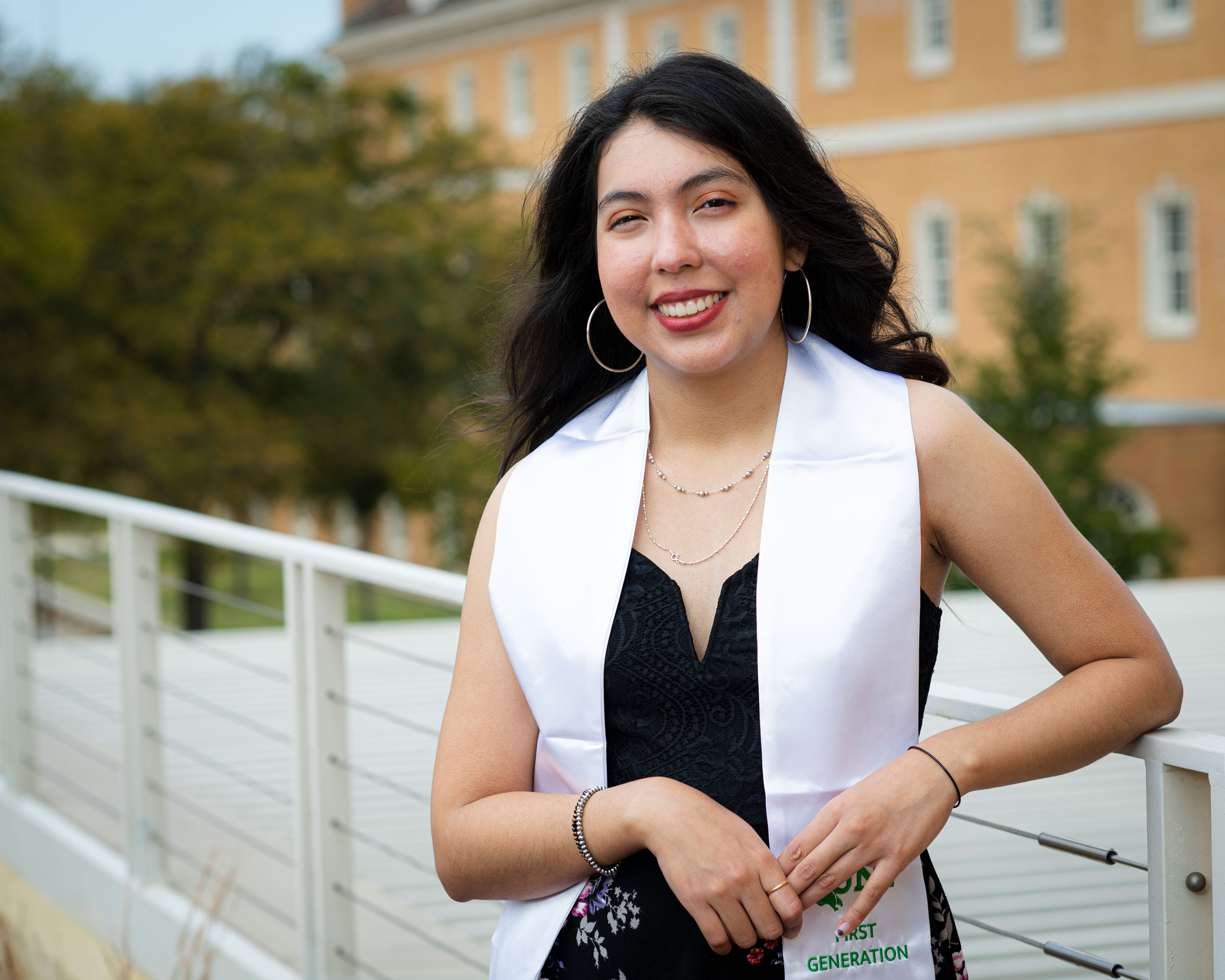 Alondra Lopez poses in front of McConnell Tower as part of a photo session for first-generation graduates at UNT.
