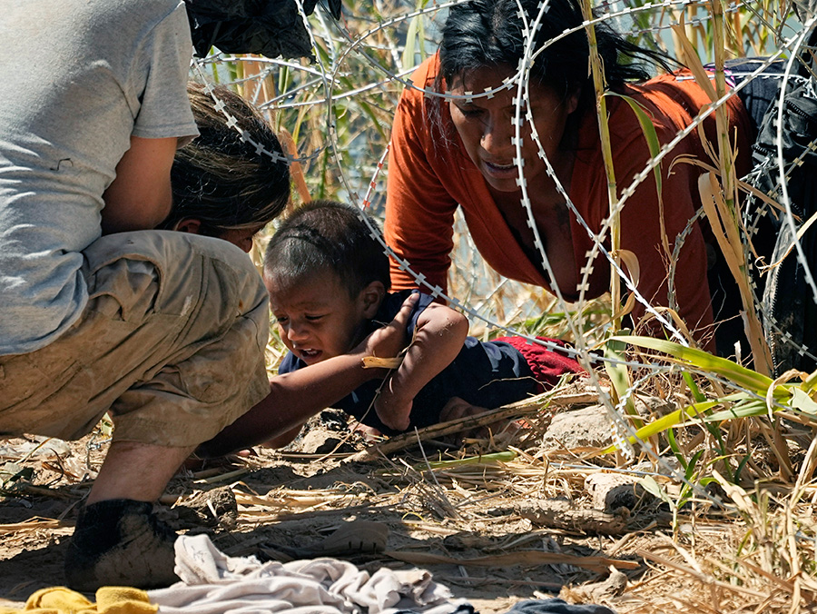 Migrants who crossed into the U.S. from Mexico pass under concertina wire