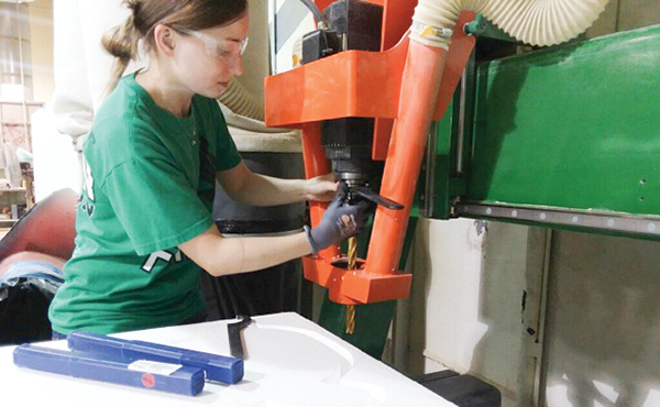Kate Sorrells wearing safety glasses an operating a large drill