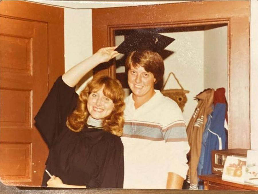 Photo of Tami and Chuck McIntire in 1981 trying on a graduation cap in their apartment 